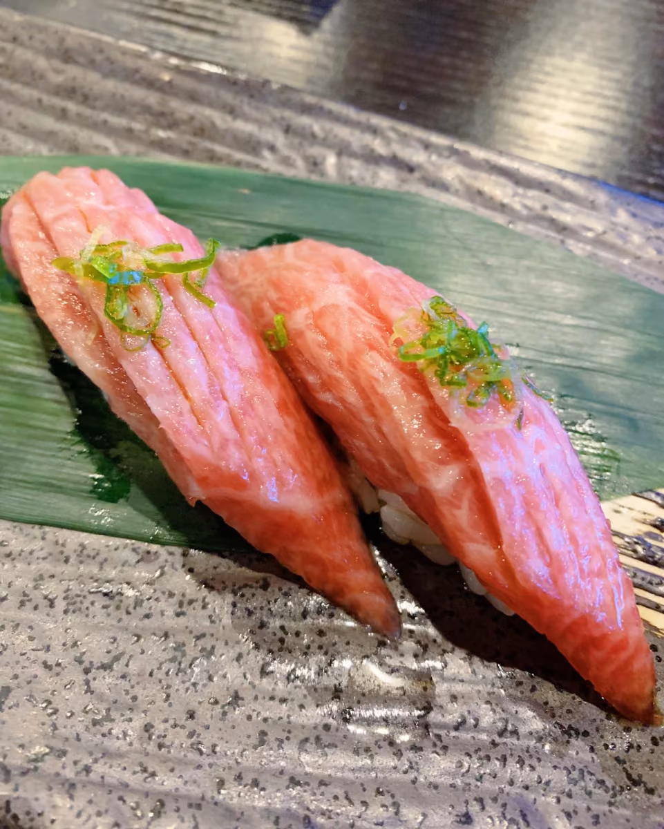 Two pieces of fish nigiri on a green leaf and ceramic plate